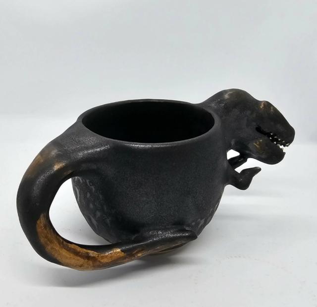 Rear view of T-Rex mug, black and brown tail at forefront with 2 arms and head visible at rear