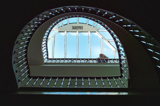 Looking upwards at the base of a fine tenement stairwell in Edinburgh. You can see blue sky and a hint of clouds through the skylight. I am at the top, peeking over the edge of the bannister.