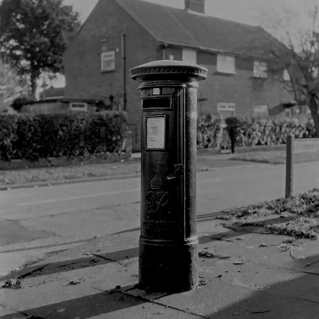 A black and white orthochromatic film photograph of a George IV postbox.