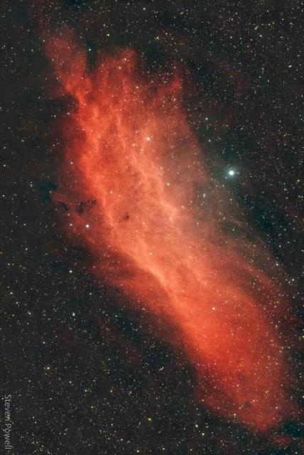 A red gaseous nebula is shown in front of a dark starfield. The shape of the nebula resembles the US state of California.