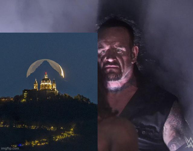 The same image NASA posted (the moon behind a mountain behind a cathedral) pasted into the meme with the Undertaker behind the image