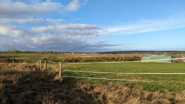 view onto a small village in the distance behind yellow-green horse pastures. the sky is blue on the right, but already overcast on the left, but it's still sunny.