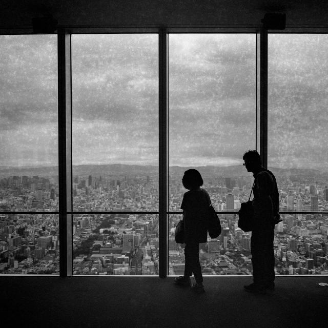 Black and white photo of a couple in silhouette in front on windows of the Harukas building at overlooking Osaka
