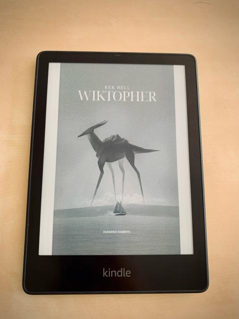 A kindle ebook reader with the WIKTOPHER book cover, written by Rek Bell and published by Hundred Rabbits