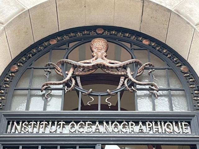A bronze octopus with its tentacles entwined in the protect bars above the steel nameplate (in cut-out lettering) of the Institut Oceanographique, in Paris.