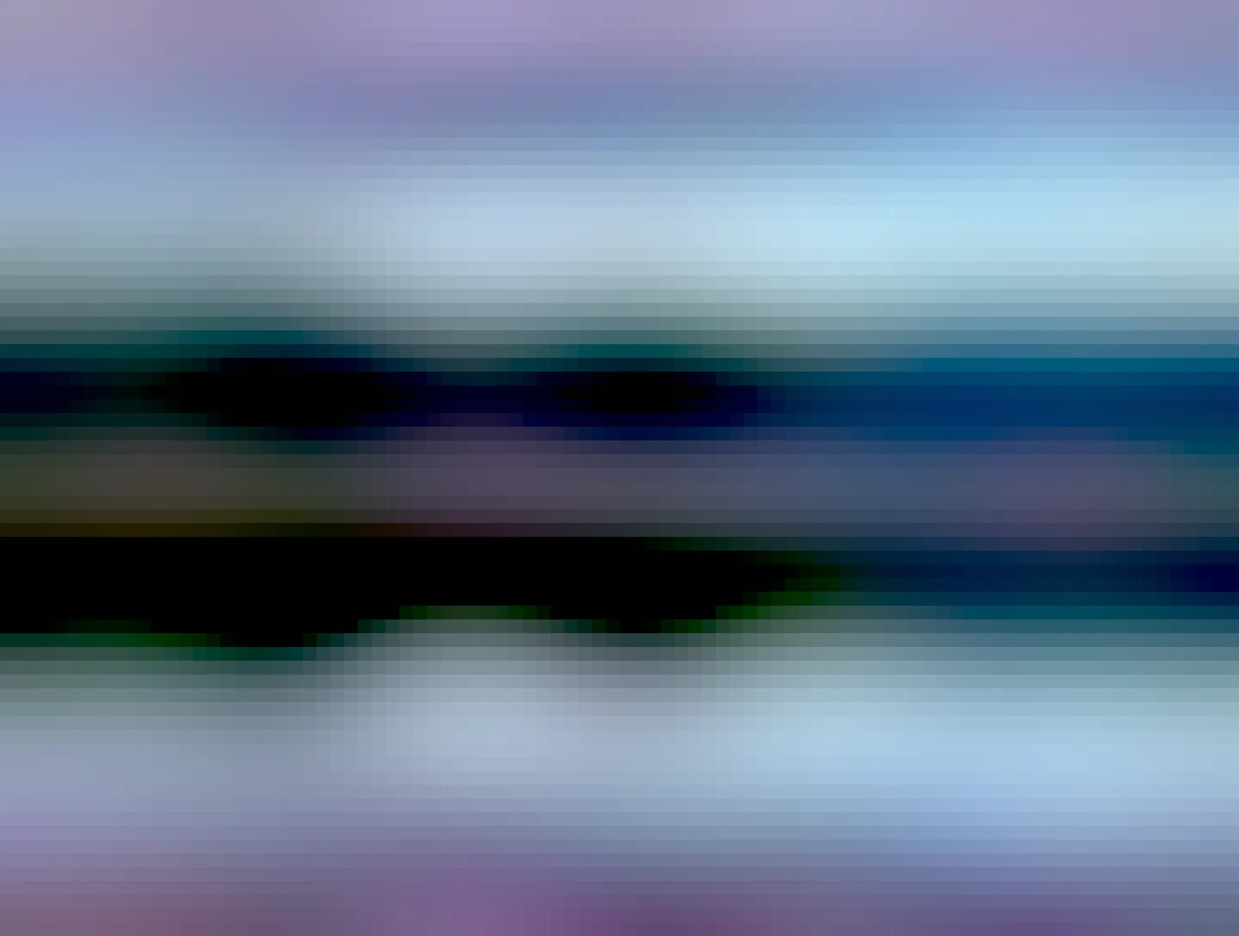 View of a nature scene with a forest in winter colours. A hill is visible in the background that still has a little snow on it. In the foreground is a river and the forest and hill are reflected in it. There are clouds on the sky and the reflection that have a pink-ish sunset hue. 