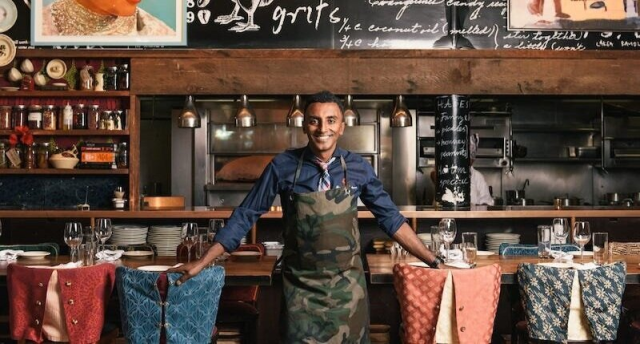 Marcus Samuelsson standing in the middle of his Red Rooster restaurant in Harlem, with the kitchen in the background behind him.