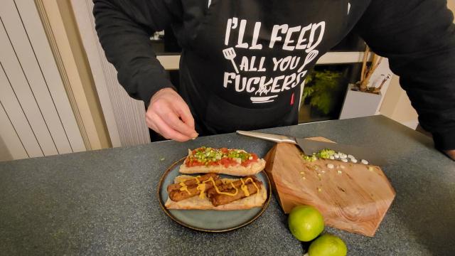 Red Onion & Rosemary Sausages on mushroom pate with a drizzle of French's mustard, on a crusty white baguette split in half with salsa & spring onions on the reverse half.
There's some bloke in the background being all check out my amazing culinary genius or something.... It's a sausage sandwich FFS.