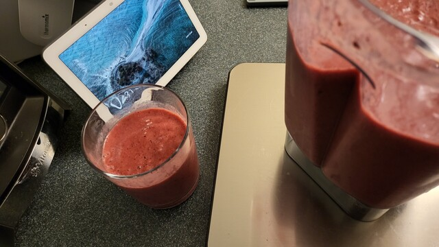 Blender and glass with smoothie on kitchen counter.