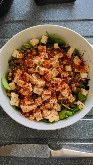 White bowl of salad part made, cubed tofu and powdered chili and spices on top, legumes and leaves underneath, not properly mixed yet.