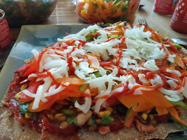 It's a flatbread base piled with juicy spicy beans salsa chunky salad with varied beans spring and white onions sliced pepers and a drizzle of sriracha over the top.