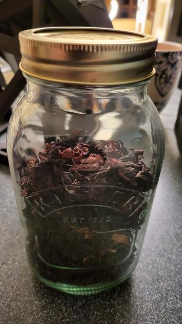 A closed glass kilner jar, viewed at an angle, with the deep purple dried hibiscus flowers inside.