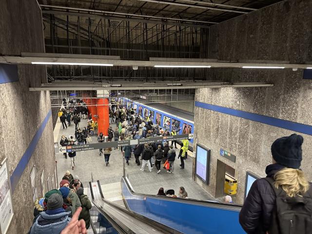 Überfüllte U-Bahn-Station von oben gesehen, mit wartenden Menschen auf dem Bahnsteig und auf Rolltreppen.