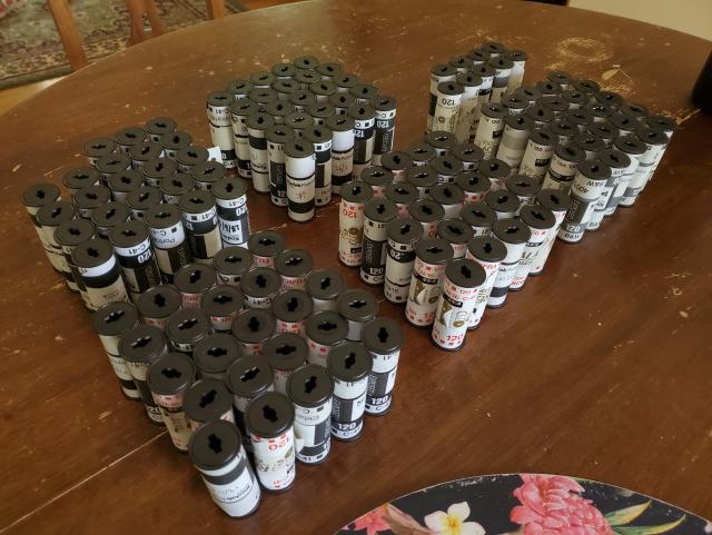 About 130 rolls of 120 film arrayed on a wooden table.