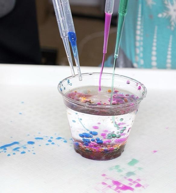 Droppers squiring colorful water into a glass of baby oil.