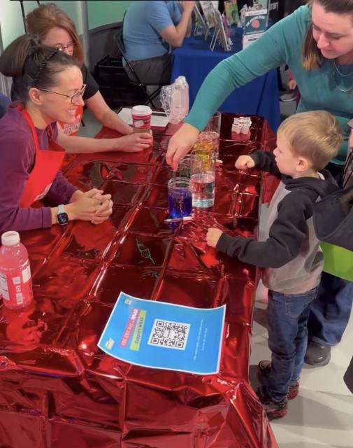 Sheril Kirshenbaum showing a young Kids Day attendee a science experiment with oil, water & food dye