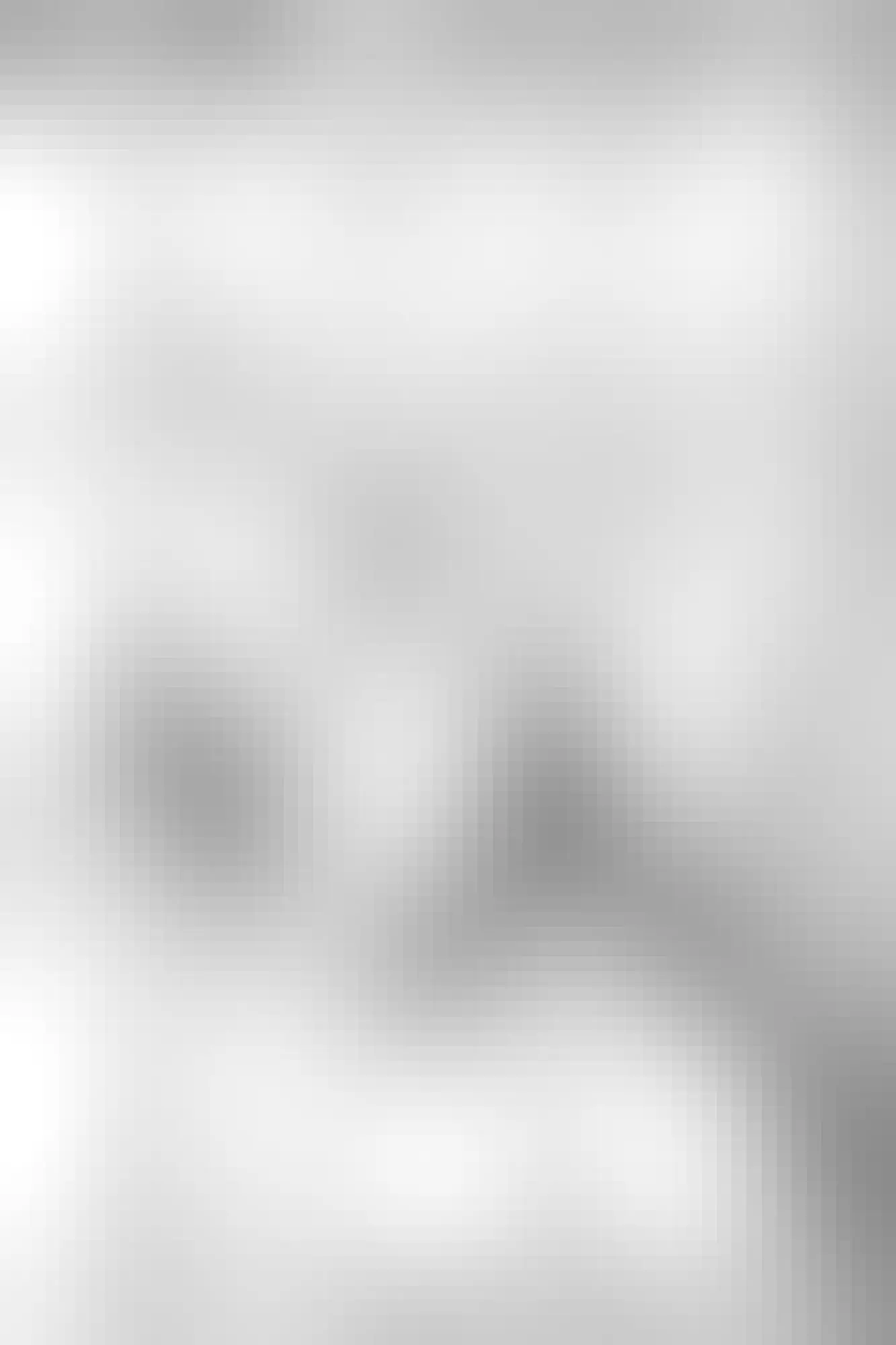 Black and white scene of a snow-covered landscape with a small stream meandering through it, featuring rounded shapes of rocks or boulders blanketed with thick snow.