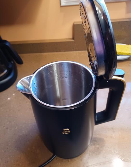 A black electric water kettle on a kitchen counter. The handle is oriented to the right and the pour spout is on the left. The lid is flipped up. On the inside, stamped into the stainless steel, two fill line markers are visible. 