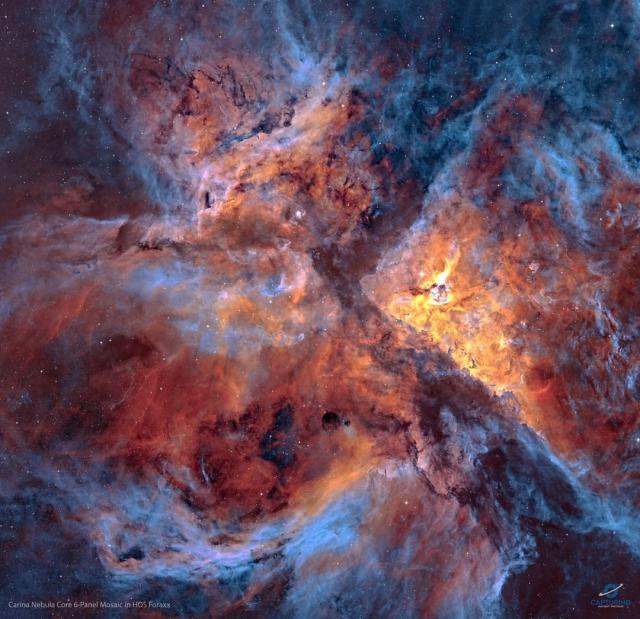 A star field strewn with filaments of dust and gas is shown: the center of the Carina Nebula. Shown in colors emitted by specific elements, the frame shows blue gas around the edges and orange and red colored gas in the center. Dark dust laces the busy frame.