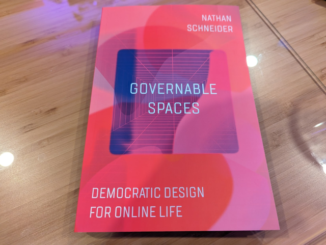 A copy of the book lies atop a bamboo desk. The cover reads: Nathan Schneider, Governable Spaces, democratic design for online life.