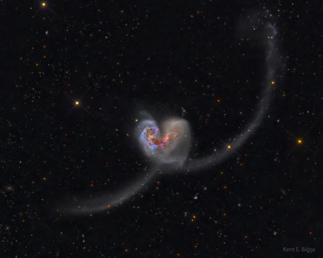 Two galaxies are seen colliding the image center. Together, they look like a classic heart icon but with long tails.