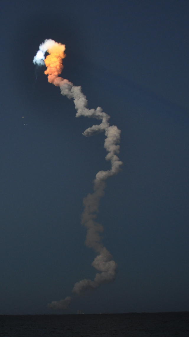 Smoke trail post Shuttle launch. The smoke casts a streaking shadow at the apex. The Shuttle and the two boosters falling away are also visible.