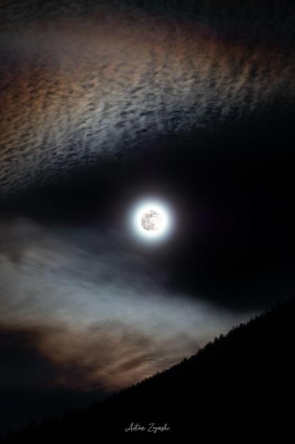 A bright full moon is seen in the center of the image. Angular clouds are seen around the edges which make the moon look like it is either in the mouth of the wolf, or the eye of a wolf.