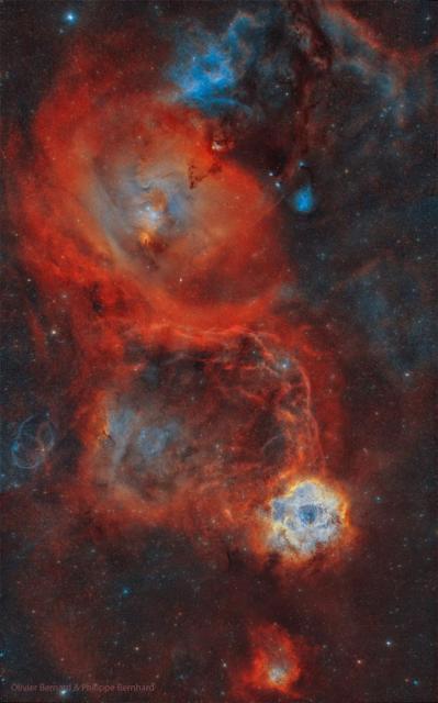 A busy star field is shown with several large red nebulae. The Rosette Nebula is among them and seen on the lower right, while the nebula surrounding the Cone Nebula is larger and visible toward the upper left.