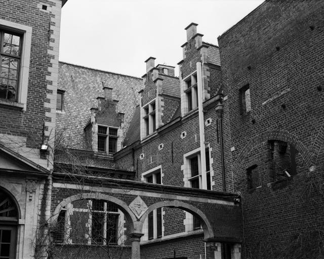 A black and white photo of a historic building made of red brick, with archways and pillars, and various embellishments.