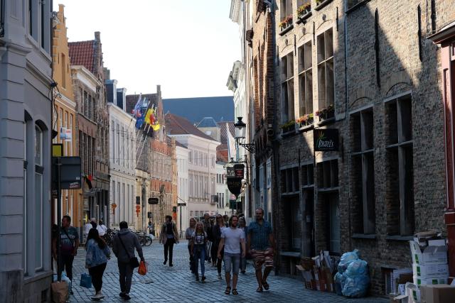 Pedetrians walking on a curved cobblestone street. There are old looking buildings and with flags. It is evening.
