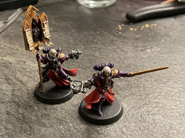 Two Adepta Sororitas miniatures painted in a purple, red and gold color scheme. 