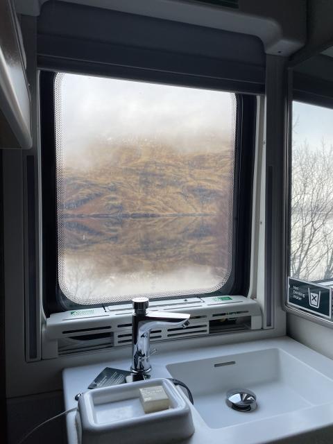 view of highland scenery out of a train cabin window . 