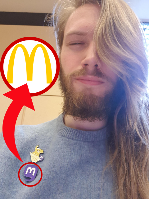 Erik Uden looking "sad" whilst wearing two Mastodon pins. The picture is edited to show a red arrow from the Mastodon pin to a McDonalds logo. 
