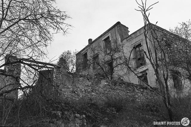 A black-and-white photo of the back of the main dwelling. The house is a two-storey structure with a second floor in the middle section. A stone wall extends out at the back, enclosing what was probably a courtyard garden.