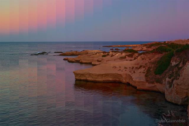 A rocky shoreline is shown with land on the right and water on the left. Above is a sky that shows unusually pixelated and colored vertical bands.