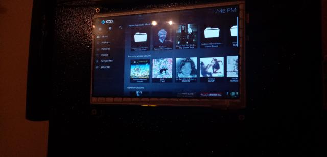 Photo of a touchscreen attached to a black box showing a music media player interface with images of album covers