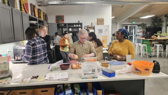 Ten people performing various cooking tasks in a brightly lit open kitchen.