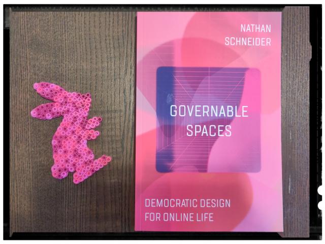 A pink and purple bunny made of melty beads next to the pink and purple cover of a book, Governable Spaces