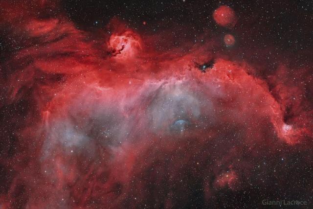 A starfield features a large nebula, mostly red, partly blue, which seems to have the shape of a bird.