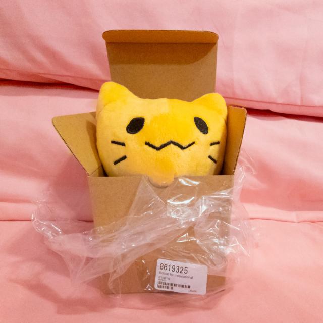 Misskeyのマスコット的な扱いを受けている、blobcat（通称にゃんぷっぷ）のぬいぐるみの写真。ピンクのシーツが敷かれたベッドの上で、元の梱包箱から突き出している。