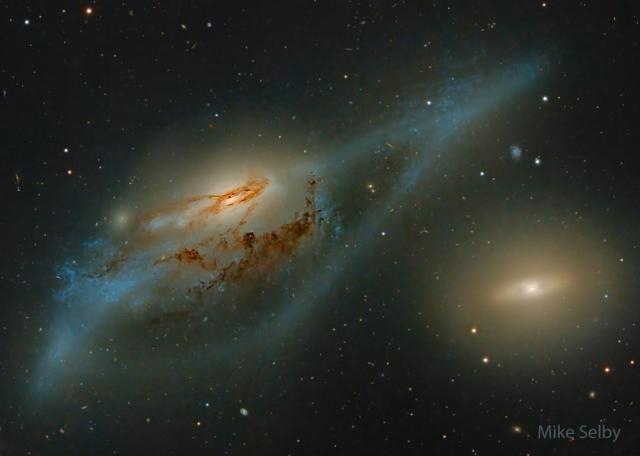 Two large galaxies are pictured. On the left is a distorted spiral galaxy, while on the right is a relatively featureless yellow disk galaxy. Together, these galaxies may look, to some, like a pair of eyes.