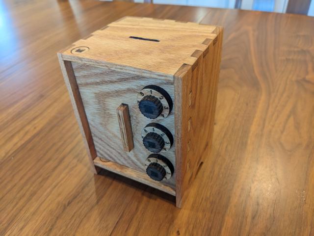 A small wooden piggybank designed to look like a bank safe. It has three dials, each with numbers 1 through 8 around the perimeter. It is currently closed.