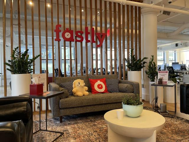 A stuffed Mastodon toy sitting on the couch of the Fastly office underneath their logo.
