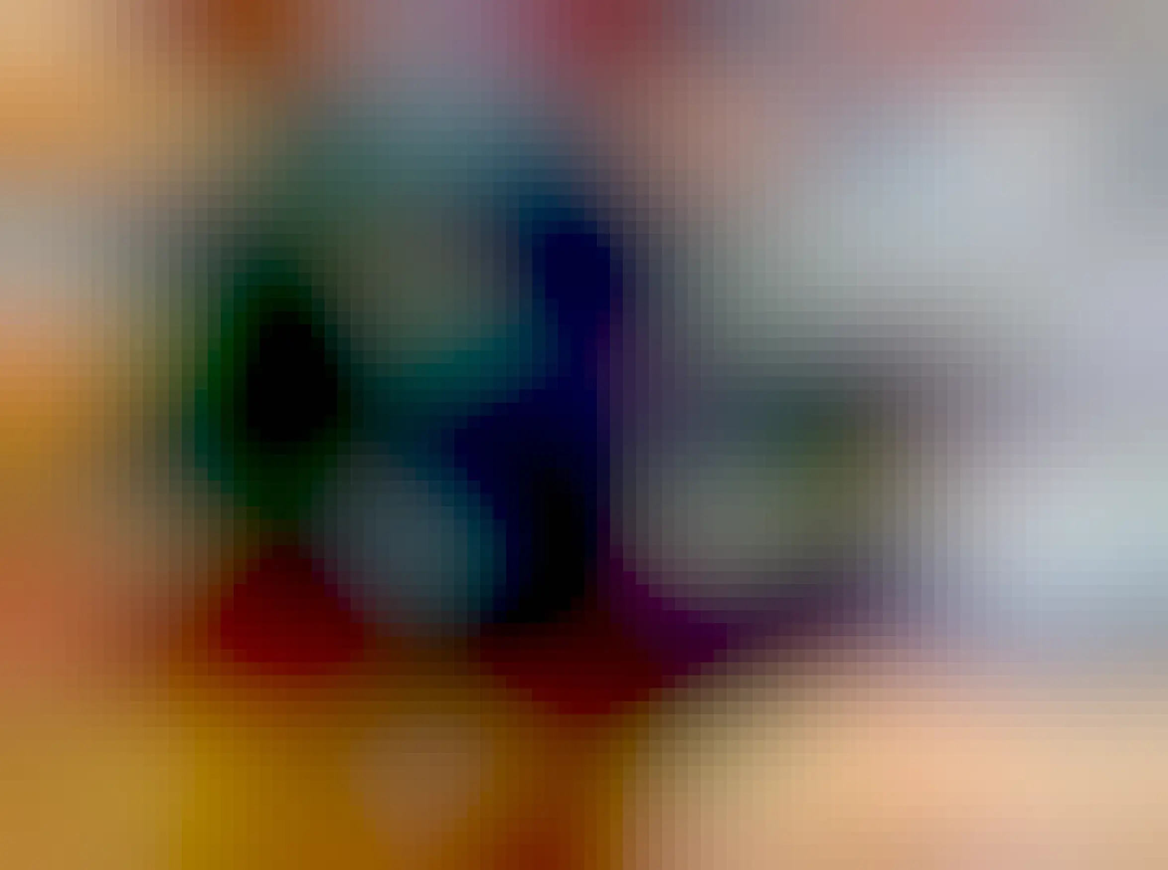 A black cat sits in a small box with low sides, overflowing and looking at the camera. 