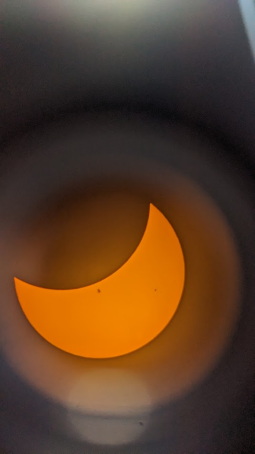 An image of a partial eclipse taken through a telescope with a solar filter. Faint sun spots are visible on the surface.