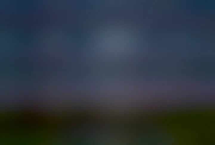  A starry sky is seen over a dark grassy landscape. Three bright objects are seen in the sky. They are Jupiter on the upper left, a crescent Moon on the upper right, and Comet Pons-Brooks below them, making a triangle. Two tails are seen extending nearly upwards from the comet.