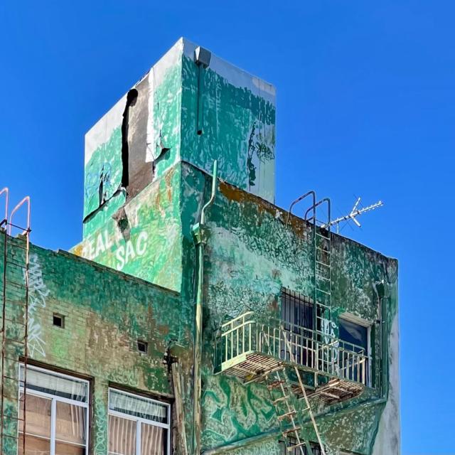 Top floors of a large building with multiple levels and sections. The green exterior paint is wearing off and exposing past layers and history