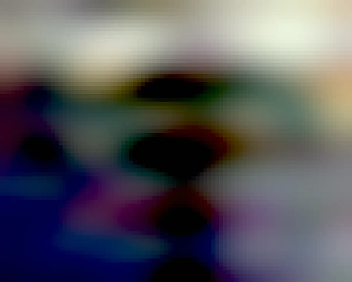 A close up of a black Toy Poodle with her chin resting on a blue jean clad ankle. There is a brown blanket with a paw print pattern on it in the  background. 