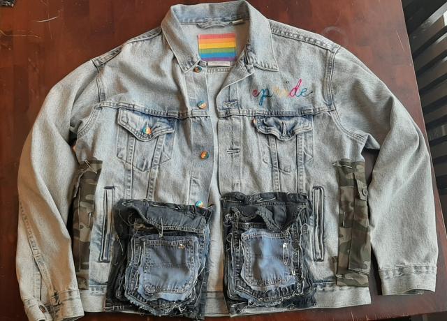 front of the levis pride jacket with rainbow buttons and tag and pride embroidery. it has two large denim cargo pockets pinned onto the front with two more layers of pockets pinned atop those