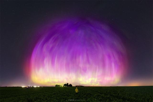  A large purple transparent dome appears to cover much of a starry sky. A person stands in a field looking toward the unusual spectacle.